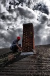 Worker inspecting chimney under cloudy sky.