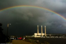 Rainbow over industrial facility near water.